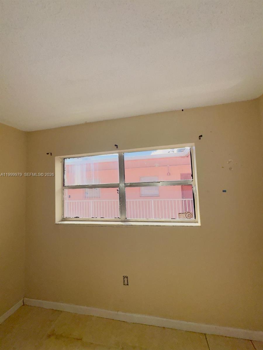 An empty room with beige walls, tile flooring, and a window looking out at a building — 19841 SW 114th Ave # 310, Miami FL 33157, MIAMI, FL