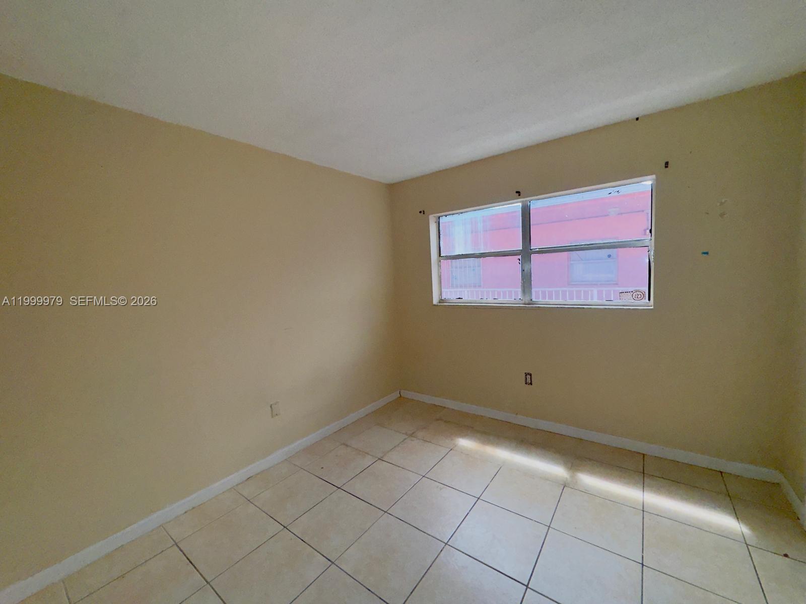 An empty room with beige walls, tile flooring, and a window overlooking a pink building — 19841 SW 114th Ave # 310, Miami FL 33157, MIAMI, FL