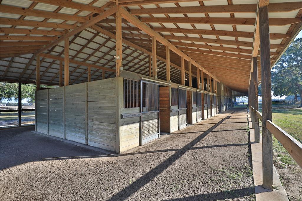 An open-air horse barn features a row of wooden stalls with metal gates and dirt flooring — 7505 SW 73RD STREET, OCALA, FL
