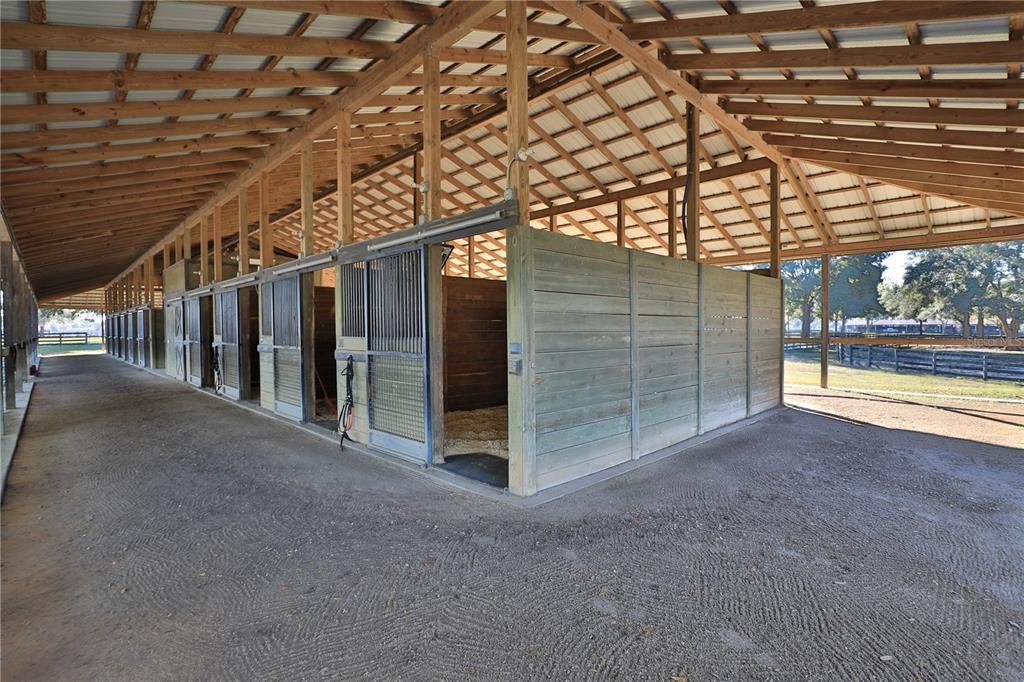An open-air horse barn features a row of stalls with sliding metal doors — 7505 SW 73RD STREET, OCALA, FL