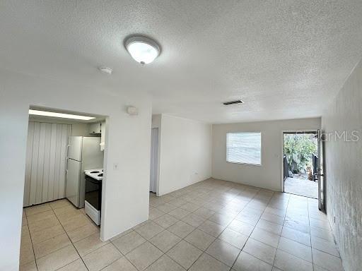An open-concept living area with tile flooring leads to a kitchen and an exterior door — 1221 KENNEDY ROAD UNIT 48, DAYTONA BEACH, FL