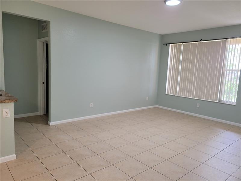 An empty room with light green walls, beige tile flooring, and a large window — 3569 Forest Hill Boulevard # 117, Palm Springs FL 33406, PALM SPRINGS, FL