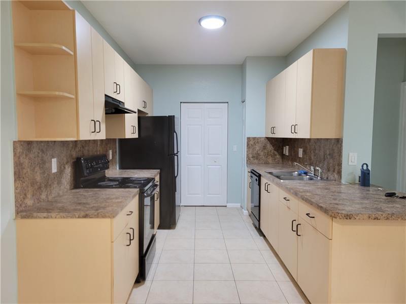 A kitchen features light wood cabinets, dark laminate countertops, black appliances, and light tile flooring — 3569 Forest Hill Boulevard # 117, Palm Springs FL 33406, PALM SPRINGS, FL