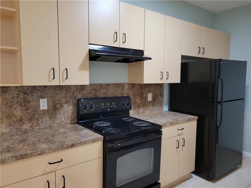 A kitchen features light wood cabinets, black appliances, and brown laminate countertops — 3569 Forest Hill Boulevard # 117, Palm Springs FL 33406, PALM SPRINGS, FL