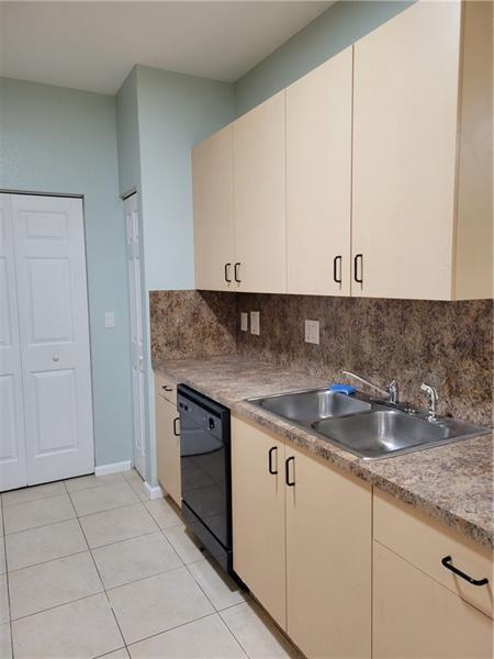 A kitchen features light-colored cabinets, a dark laminate countertop, a double sink, and tile flooring — 3569 Forest Hill Boulevard # 117, Palm Springs FL 33406, PALM SPRINGS, FL