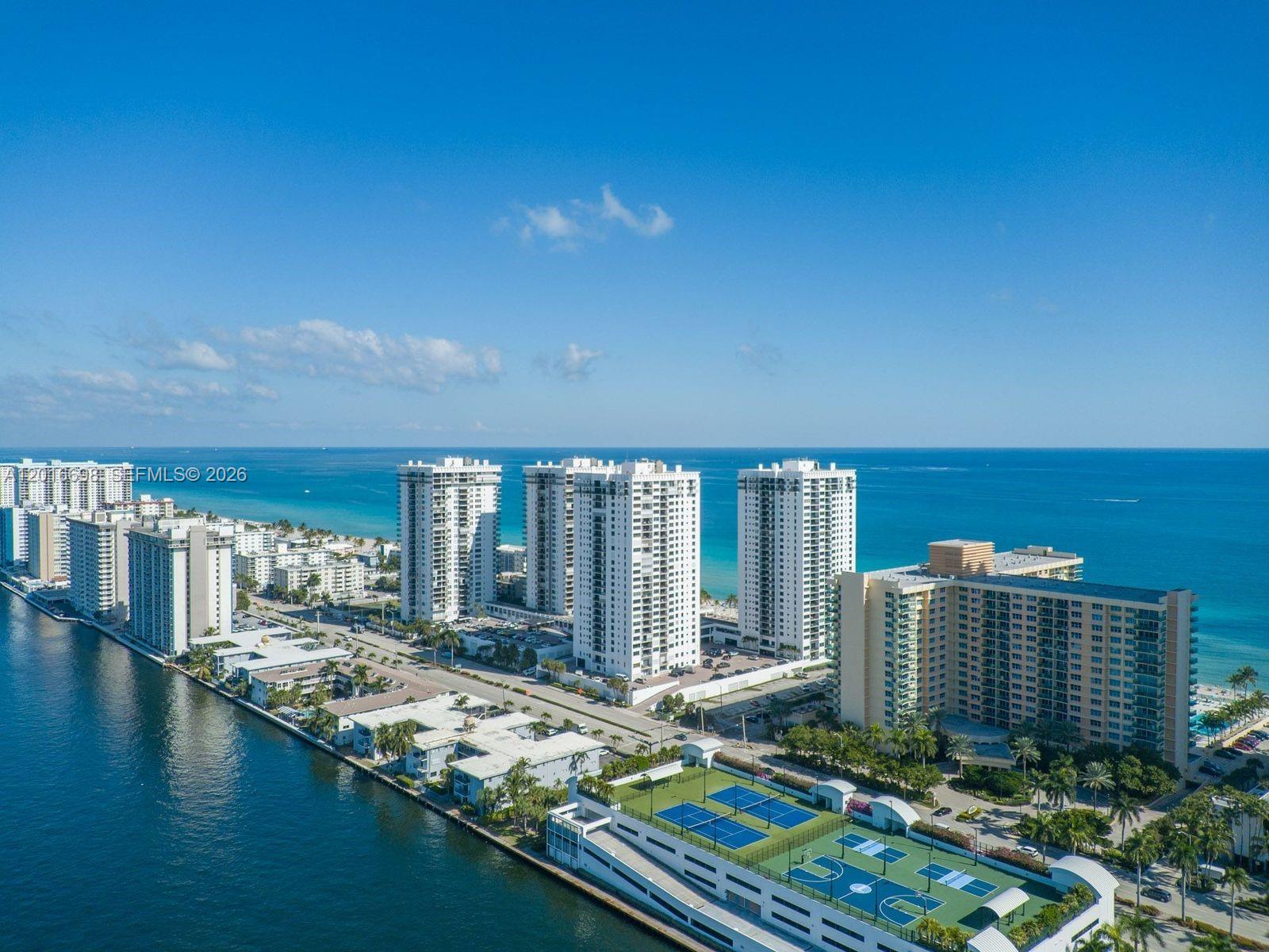 An aerial view shows high-rise apartment buildings along a coastline with tennis courts in the foreground — 2501 S Ocean Dr, Hollywood FL 33019, HOLLYWOOD, FL