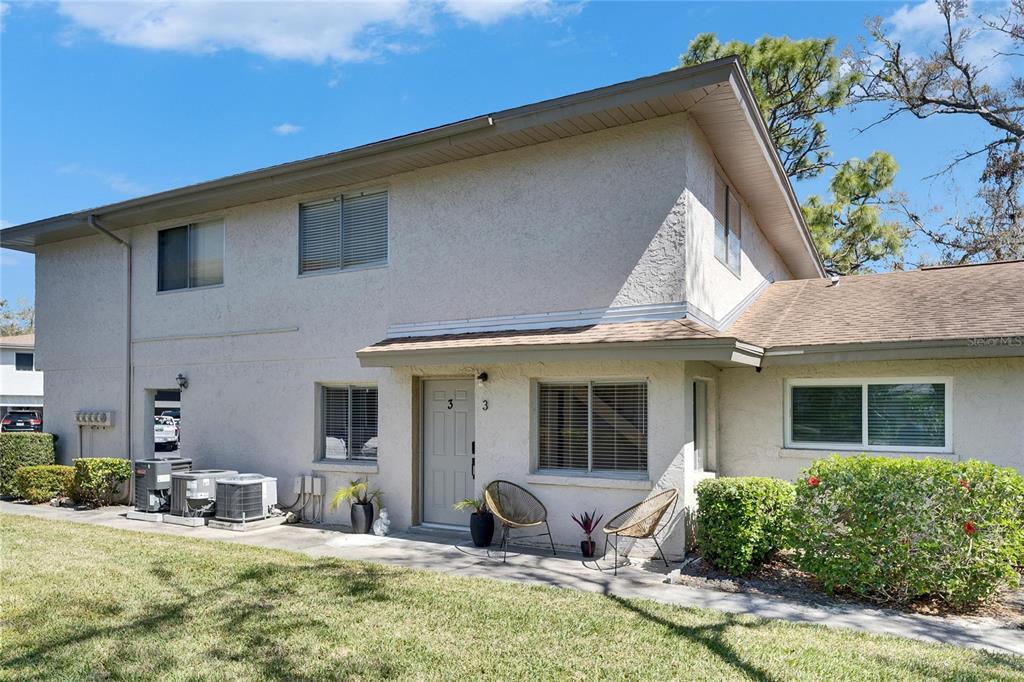 A two-story stucco building exterior features a ground-level entrance with two chairs and landscaping — 1828 BOUGH AVENUE UNIT 3, CLEARWATER, FL