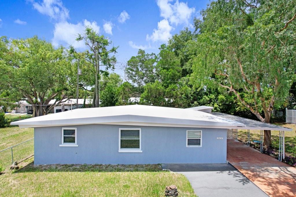 A single-story light blue house with a flat roof and an attached carport — 39038 HEATH DRIVE, ZEPHYRHILLS, FL