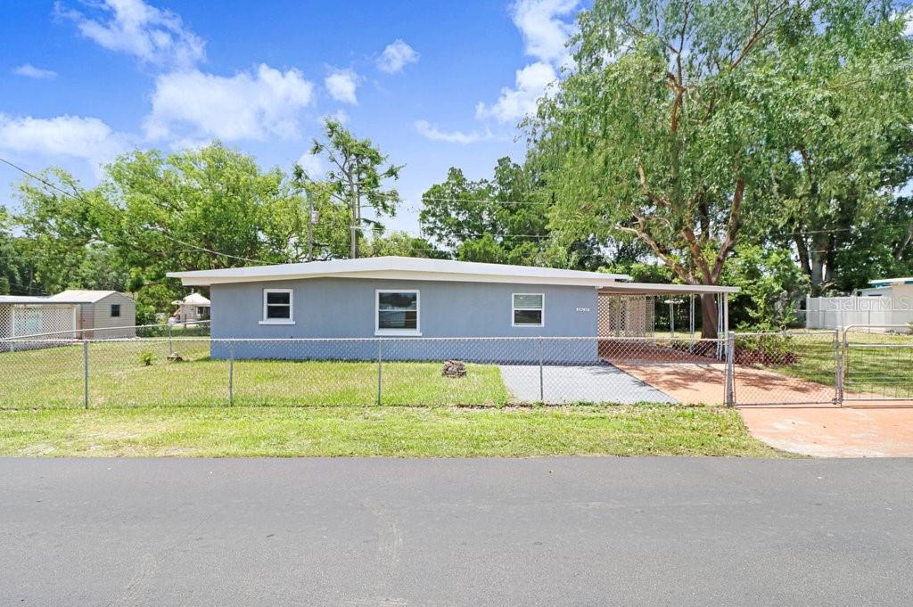A single-story gray house with a flat roof sits behind a chain-link fence — 39038 HEATH DRIVE, ZEPHYRHILLS, FL