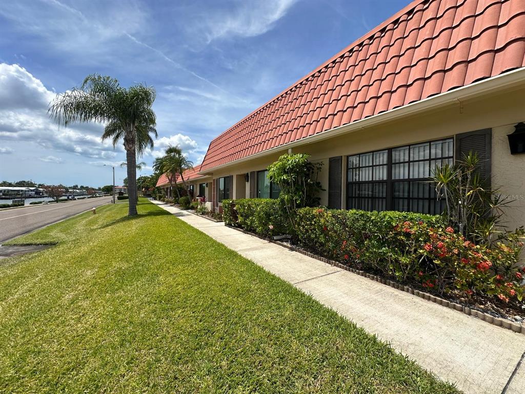 A low-rise building with a red tile roof sits beside a sidewalk and grassy lawn — 19029 US HIGHWAY 19 N UNIT 21F, CLEARWATER, FL
