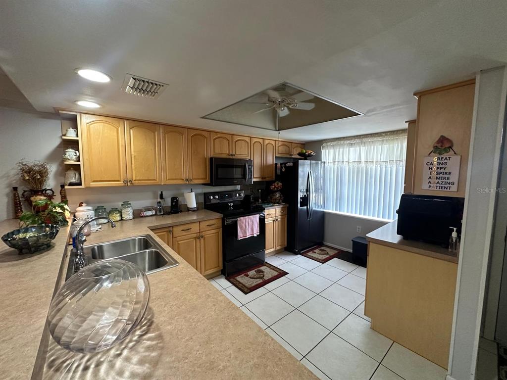 A kitchen features light wood cabinets, black appliances, a double sink, and tiled flooring — 19029 US HIGHWAY 19 N UNIT 21F, CLEARWATER, FL