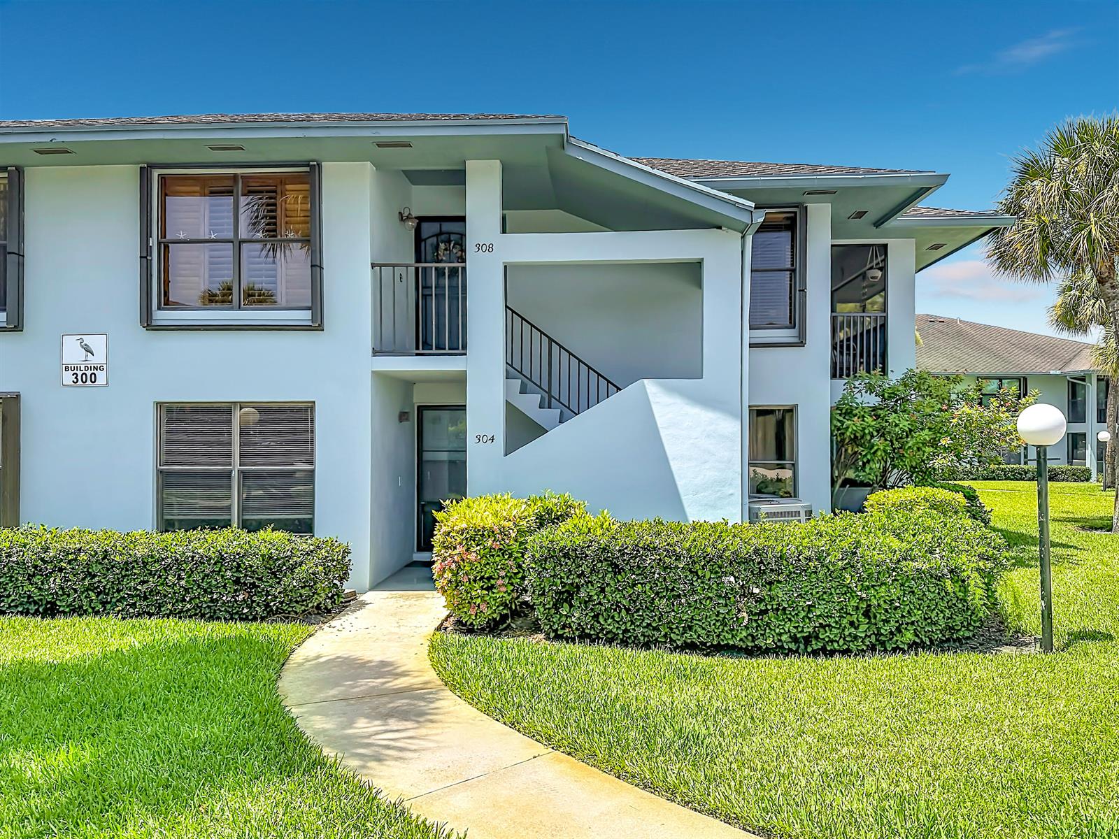 A two-story apartment building exterior features a walkway, manicured hedges, and numbered unit entrances — 950 S Kanner Highway # 308, Stuart FL 34994, STUART, FL