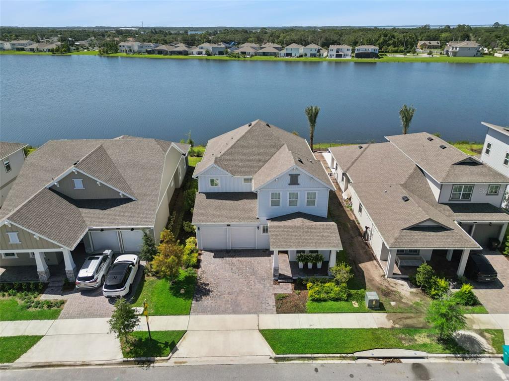 An aerial view shows three suburban houses situated along a lakefront with paved driveways — 13557 MCMILLAN DRIVE, ORLANDO, FL
