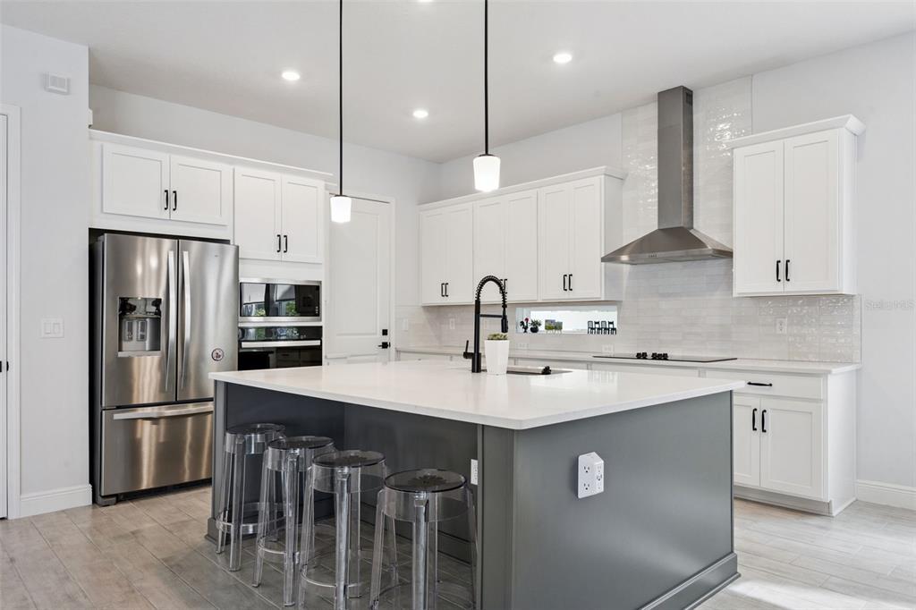 A modern kitchen features white cabinets, a gray island with bar stools, and stainless appliances — 13557 MCMILLAN DRIVE, ORLANDO, FL