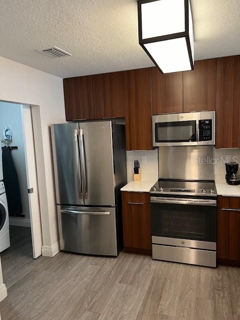 A kitchen features stainless steel appliances, dark wood cabinetry, and light wood-look flooring — 14501 GROVE RESORT AVENUE UNIT 3714, WINTER GARDEN, FL