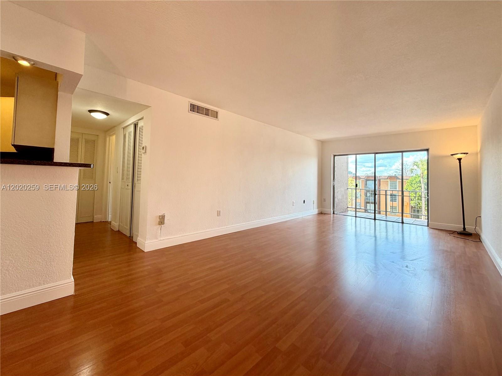 An empty living room features wood-look flooring, white walls, and a sliding glass door balcony — 9429 SW 76th St # W38, Miami FL 33173, MIAMI, FL
