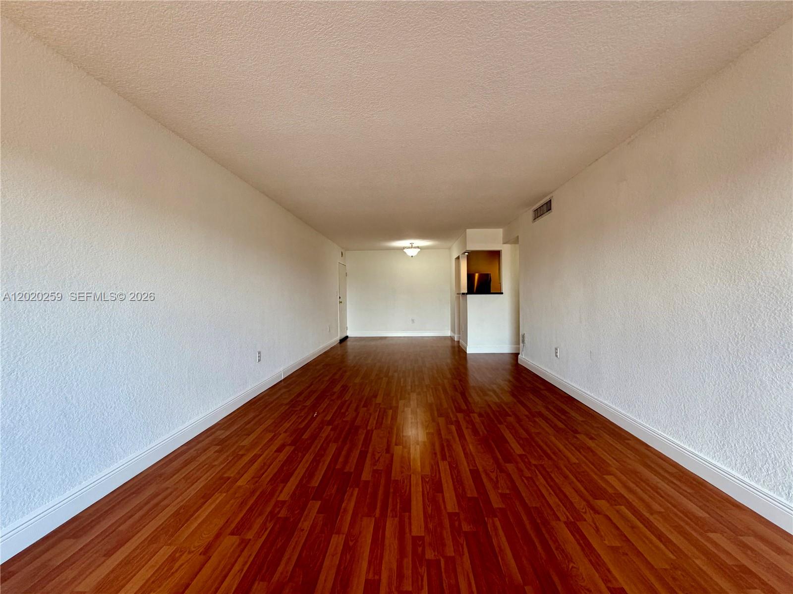 An empty living room features white walls, wood-look flooring, and a small kitchen pass-through — 9429 SW 76th St # W38, Miami FL 33173, MIAMI, FL