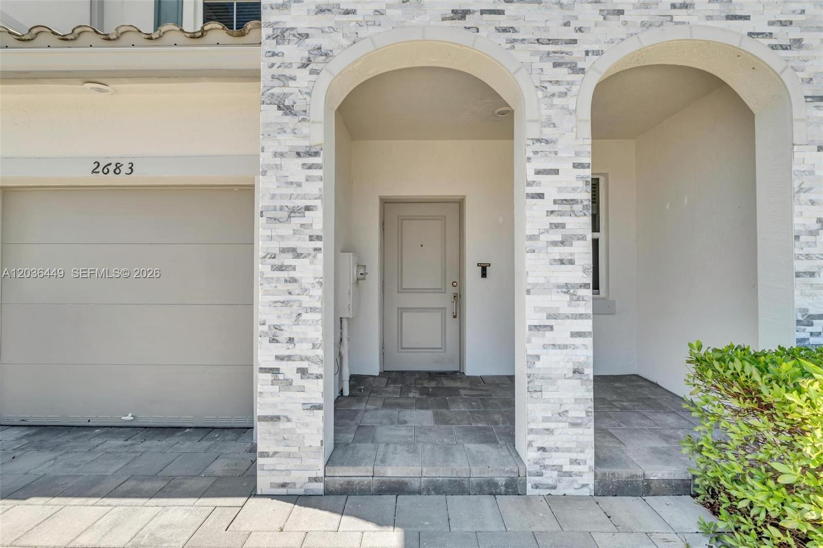 A stone-clad arched entryway leads to a light gray front door next to a garage — 2683 SE 12th St, Homestead FL 33035, HOMESTEAD, FL