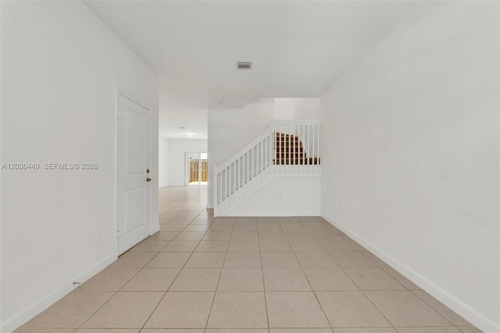 An empty room features white walls, light-colored tile flooring, and a staircase with white railings — 2683 SE 12th St, Homestead FL 33035, HOMESTEAD, FL