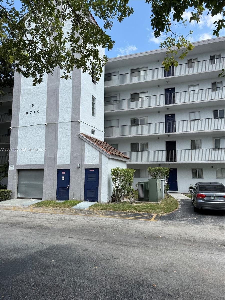 A multi-story apartment building with a white facade, gray accents, and a gray car parked nearby — 8710 N Sherman Cir # 506, Miramar FL 33025, MIRAMAR, FL