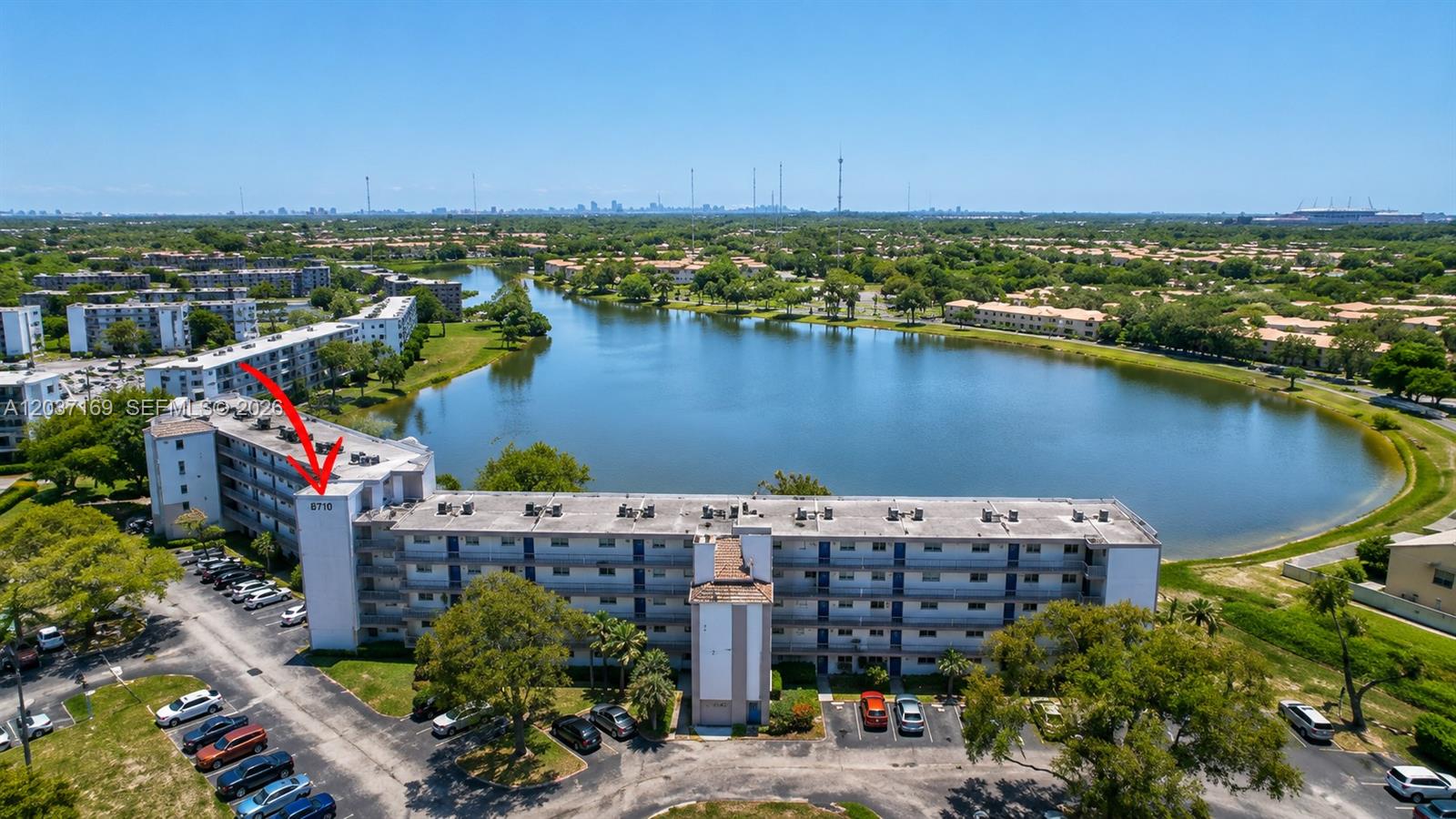 An aerial view shows a multi-story apartment building situated next to a large lake — 8710 N Sherman Cir # 506, Miramar FL 33025, MIRAMAR, FL