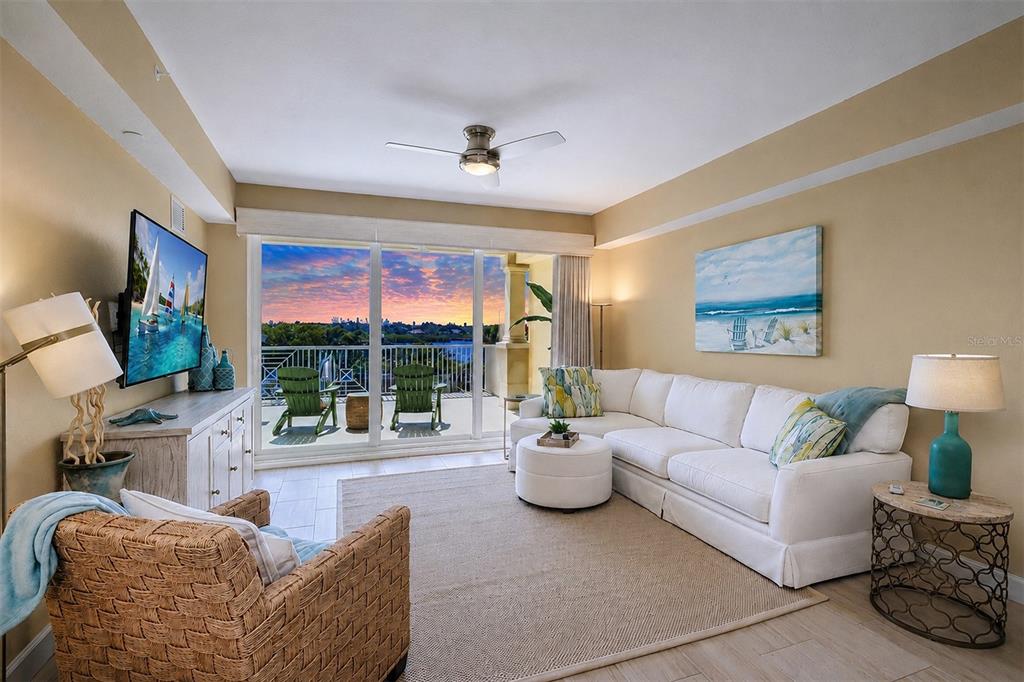 A living room features a white sectional sofa, a wicker armchair, and a balcony view — 19519 GULF BOULEVARD UNIT 202, INDIAN SHORES, FL