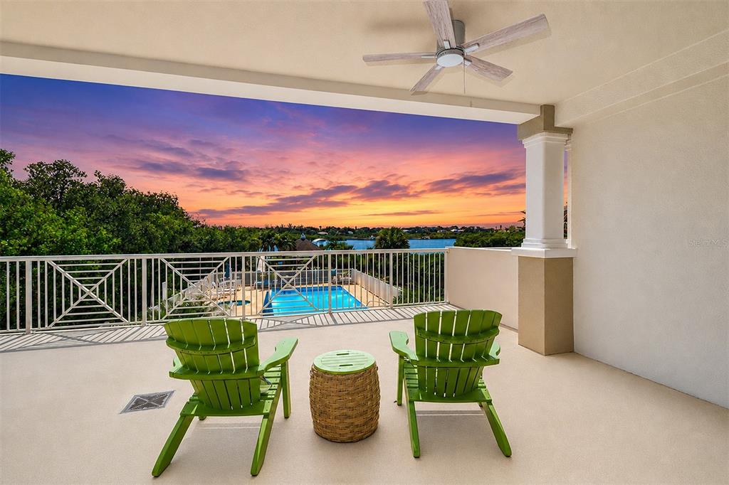 A covered balcony features two green chairs, a small table, and a view of a pool — 19519 GULF BOULEVARD UNIT 202, INDIAN SHORES, FL