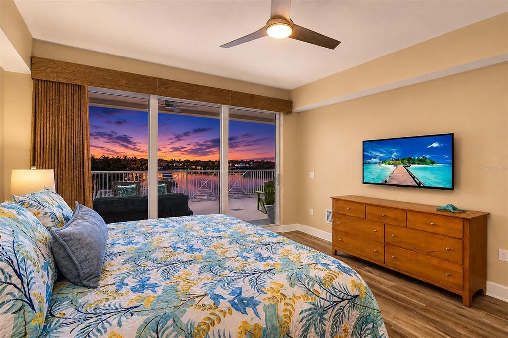 A bedroom features a floral bedspread, a wooden dresser with a television, and a balcony view — 19519 GULF BOULEVARD UNIT 202, INDIAN SHORES, FL
