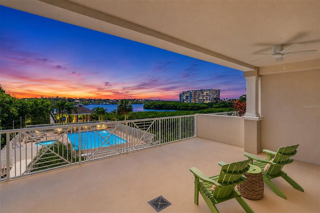 A covered balcony features two green chairs, a small table, and a view of a pool — 19519 GULF BOULEVARD UNIT 202, INDIAN SHORES, FL