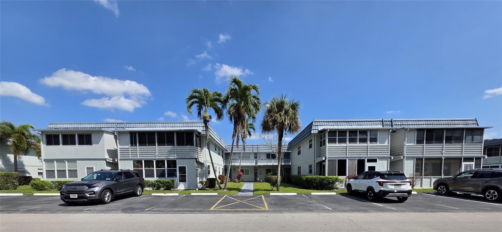 A two-story apartment complex with palm trees and a parking lot in the foreground — 216 Tuscany # D, Delray Beach FL 33446, DELRAY BEACH, FL