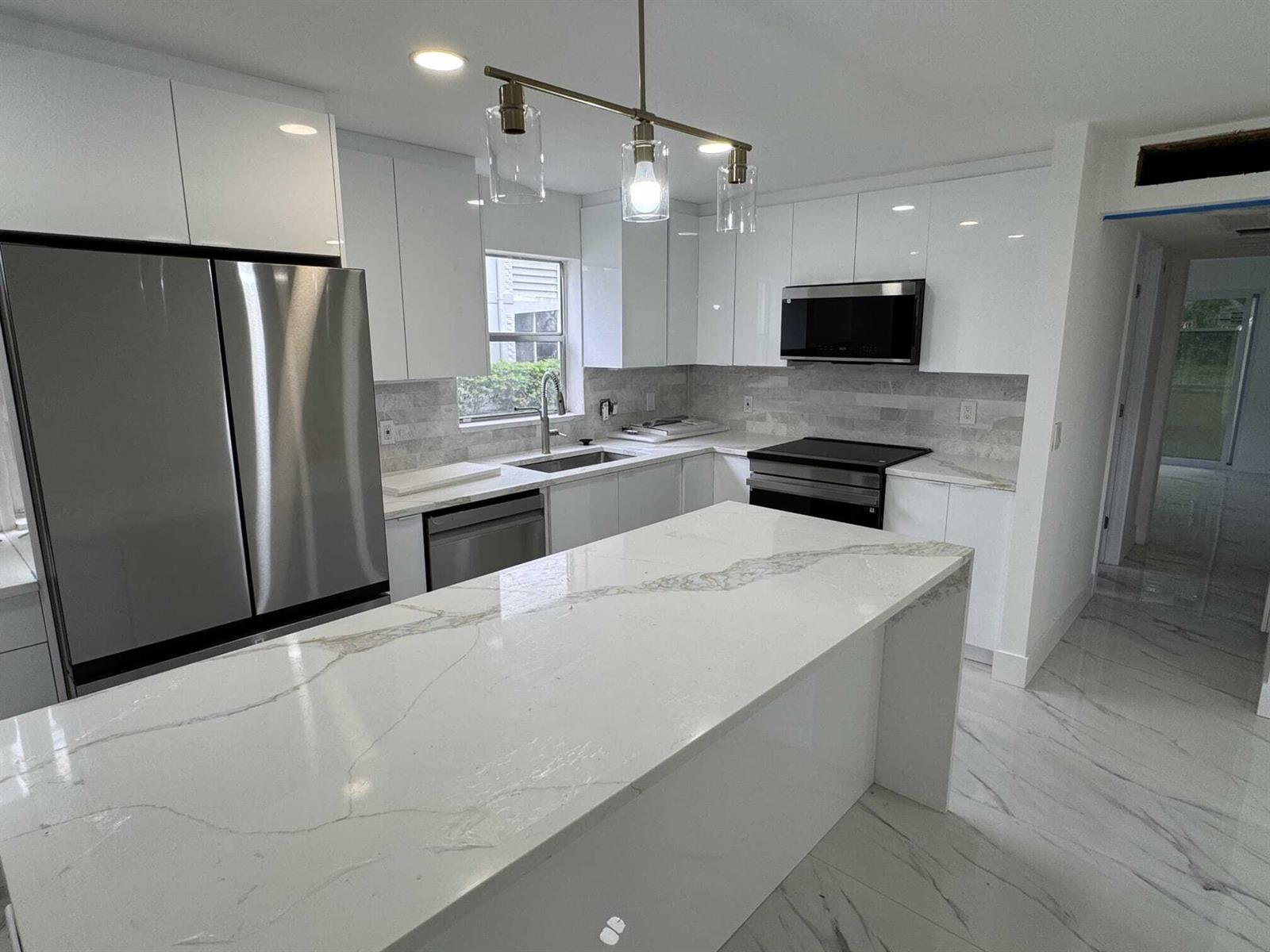 A modern kitchen features white glossy cabinets, a marble-patterned island, and stainless steel appliances — 216 Tuscany # D, Delray Beach FL 33446, DELRAY BEACH, FL