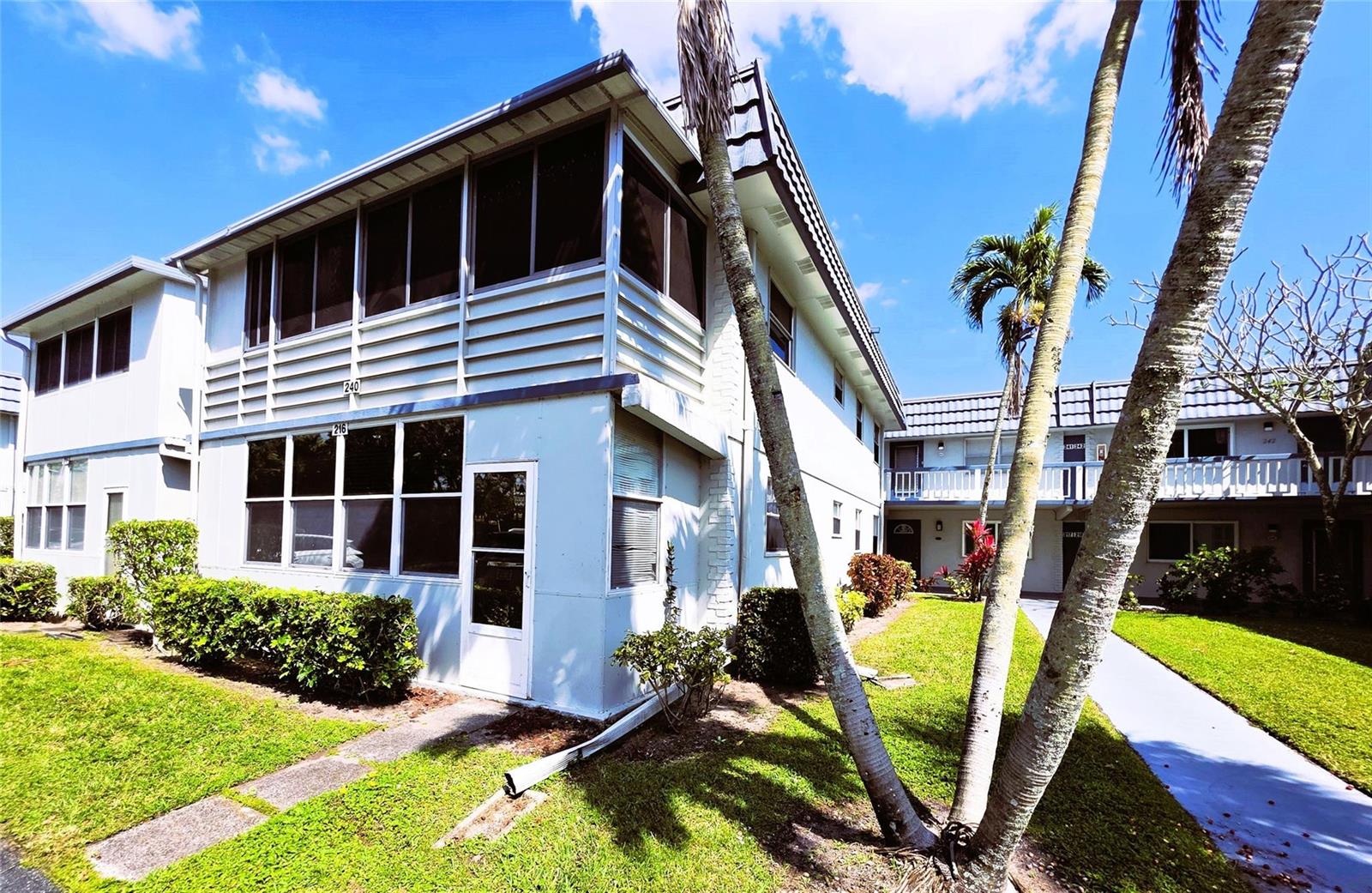 A two-story apartment building with screened balconies, white siding, and palm trees on the lawn — 216 Tuscany # D, Delray Beach FL 33446, DELRAY BEACH, FL