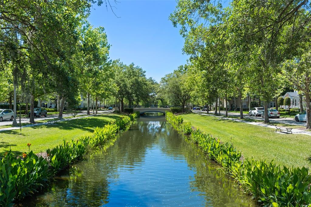A narrow canal flows through a tree-lined residential street toward a small arched bridge — 403 WATER STREET, CELEBRATION, FL