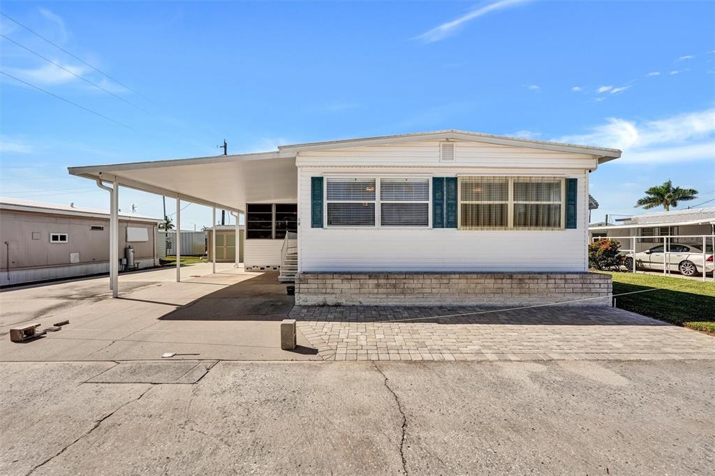 A white mobile home features a carport, brick skirting, and a paved driveway — 10315 CORTEZ ROAD W UNIT 19H, BRADENTON, FL