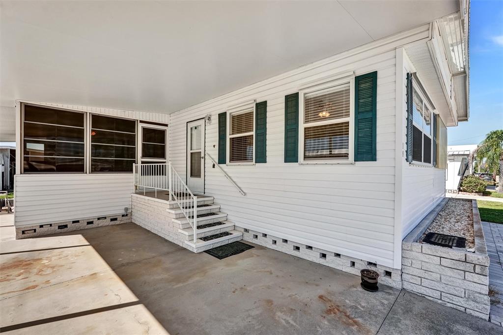 A white mobile home exterior features a covered concrete patio, stairs, and green window shutters — 10315 CORTEZ ROAD W UNIT 19H, BRADENTON, FL