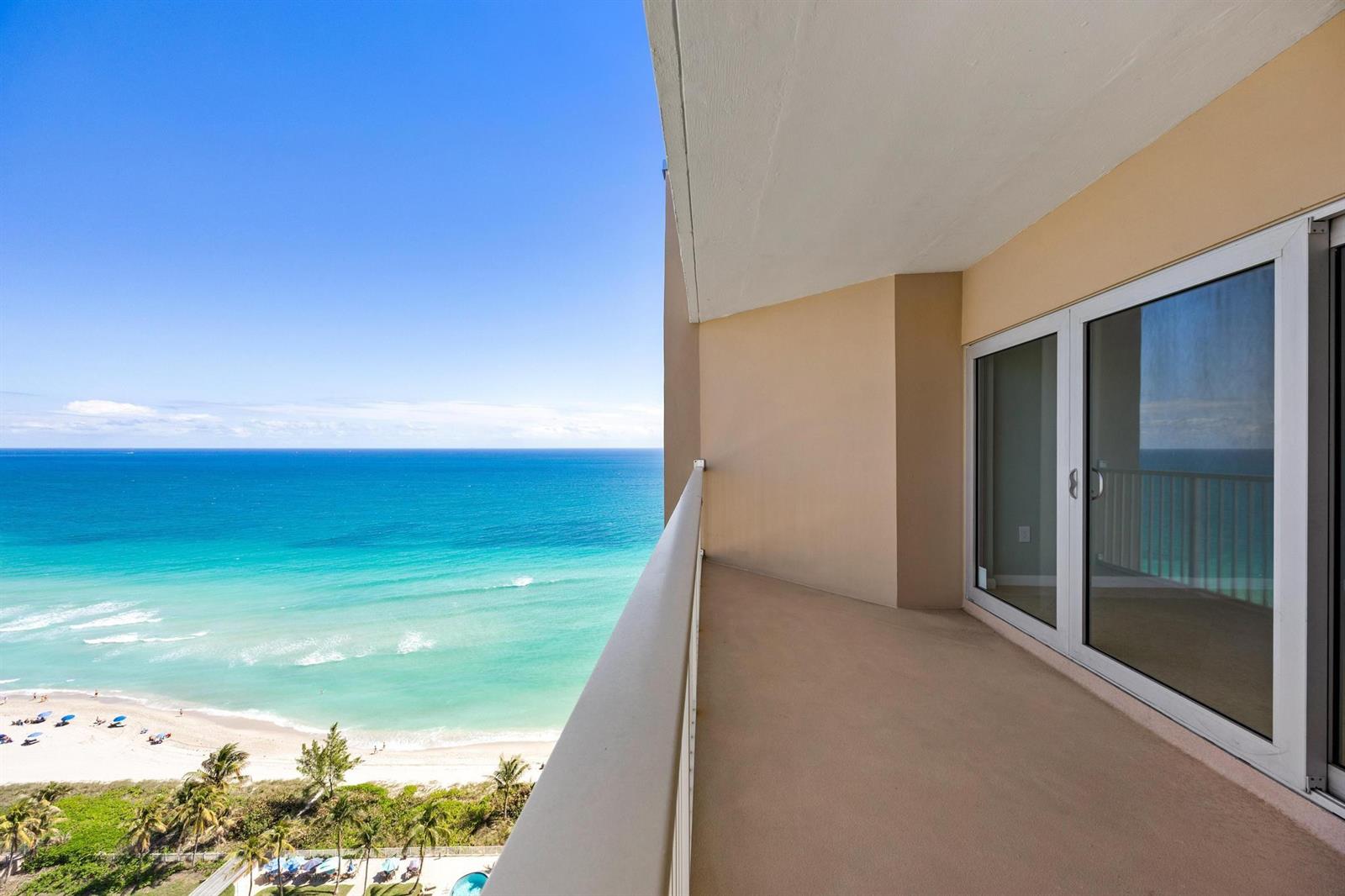 A high-rise balcony overlooks a sandy beach and the turquoise ocean under a clear sky — 1950 S Ocean Drive, Hallandale Beach FL 33009, HALLANDALE BEACH, FL