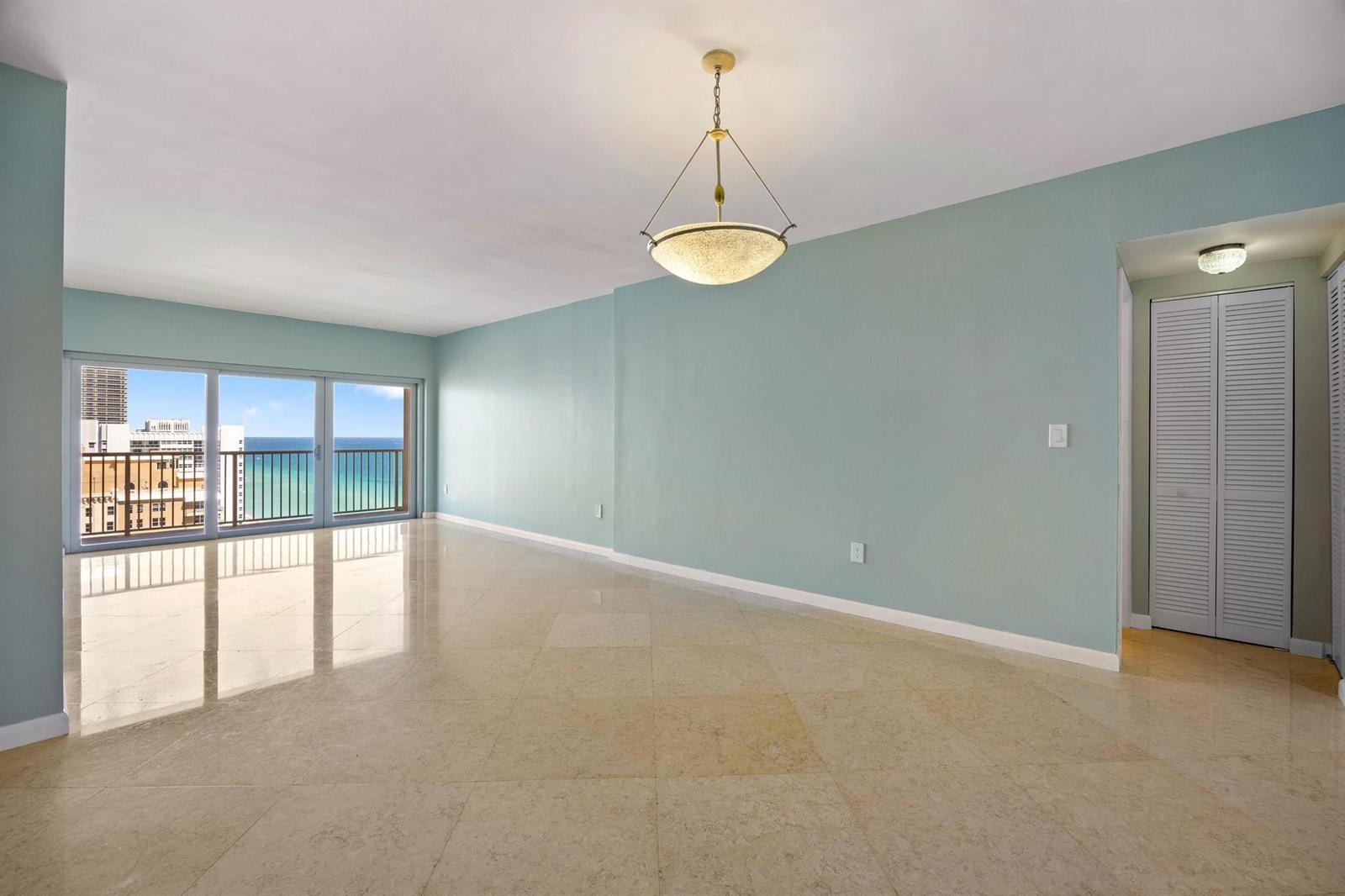 An empty living room with light blue walls, beige tile floors, and a balcony view — 1950 S Ocean Drive, Hallandale Beach FL 33009, HALLANDALE BEACH, FL
