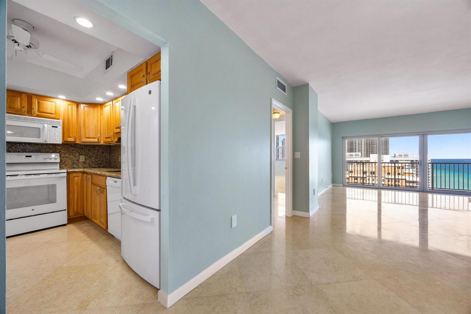 A kitchen with wood cabinets and white appliances opens to a living area with ocean views — 1950 S Ocean Drive, Hallandale Beach FL 33009, HALLANDALE BEACH, FL