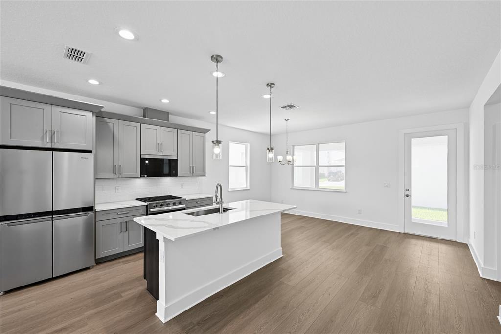 A modern kitchen features grey cabinets, white quartz countertops, a center island, and wood flooring — 1582 RIDGEBACK DRIVE, APOPKA, FL