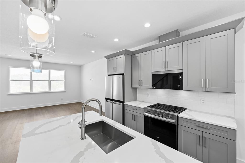 A modern kitchen features gray cabinets, stainless steel appliances, and a white quartz island countertop — 1582 RIDGEBACK DRIVE, APOPKA, FL