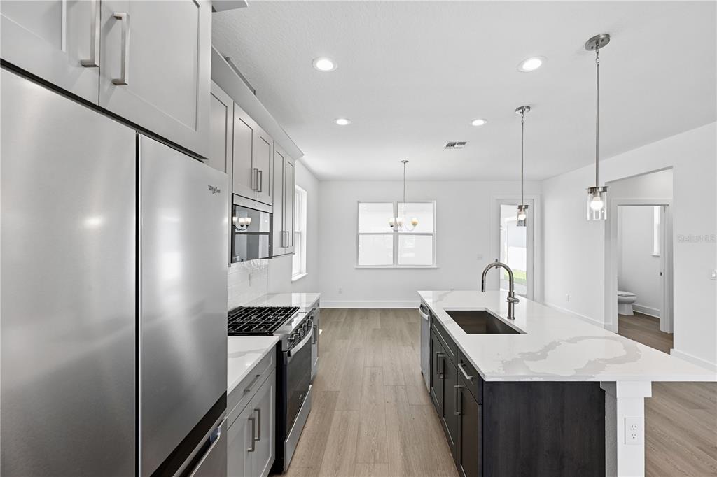 A modern kitchen features white upper cabinets, dark lower cabinets, a central island, and stainless appliances — 1582 RIDGEBACK DRIVE, APOPKA, FL
