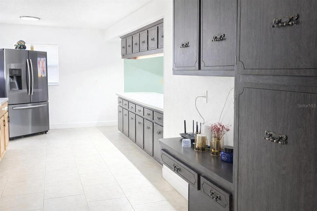 A kitchen features dark gray cabinetry, stainless steel appliances, and light-colored tile flooring — 1910 LITHIA PINECREST ROAD, VALRICO, FL