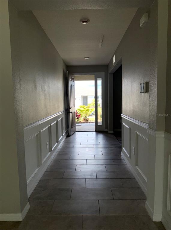 A hallway with wainscoting and tile flooring leads to an open front door — 17625 CANTARINA COVE, BRADENTON, FL