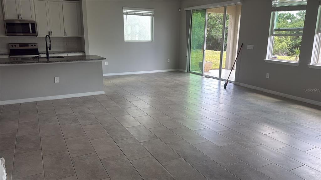 An open-concept living area features gray tile flooring, a kitchen island, and sliding glass doors — 17625 CANTARINA COVE, BRADENTON, FL
