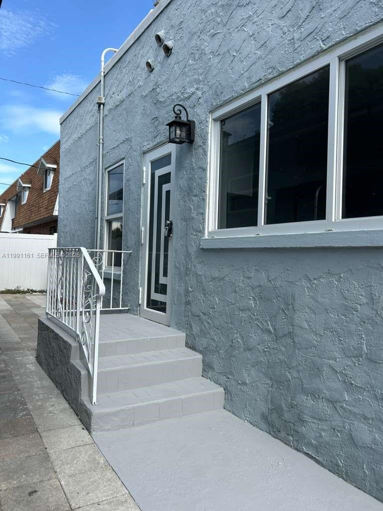 A gray stucco exterior wall features a white metal railing, concrete steps, and a door — 2242 Polk St # 2, Hollywood FL 33020, HOLLYWOOD, FL