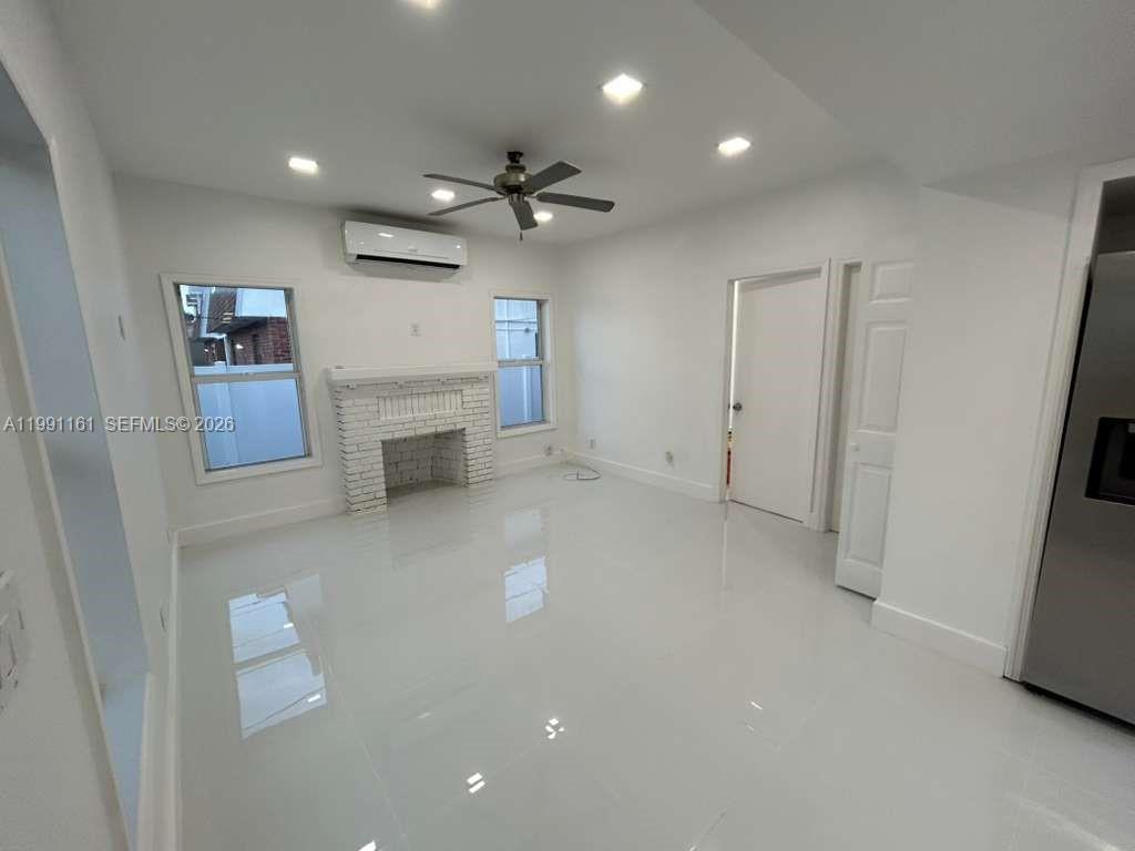 A bright living room features white tile floors, a brick fireplace, and a ceiling fan — 2242 Polk St # 2, Hollywood FL 33020, HOLLYWOOD, FL