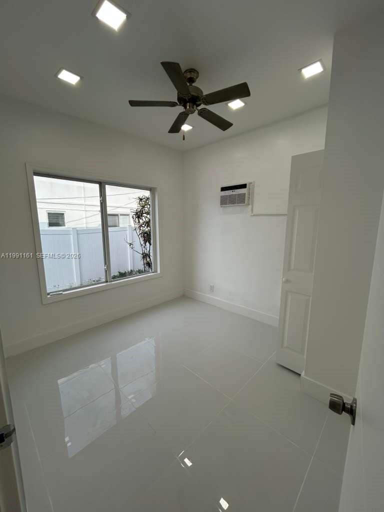 A bright, empty room features white tile floors, a ceiling fan, and a window — 2242 Polk St # 2, Hollywood FL 33020, HOLLYWOOD, FL