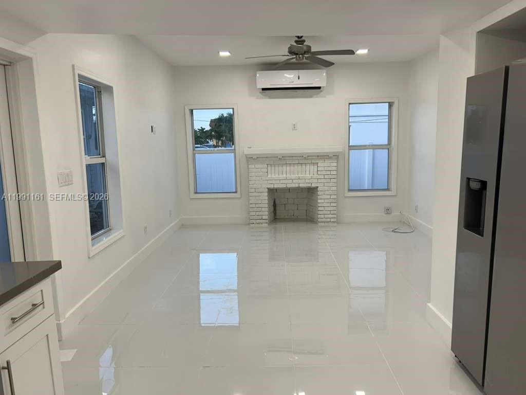 A bright living room features white tile floors, a brick fireplace, and a ceiling fan — 2242 Polk St # 2, Hollywood FL 33020, HOLLYWOOD, FL