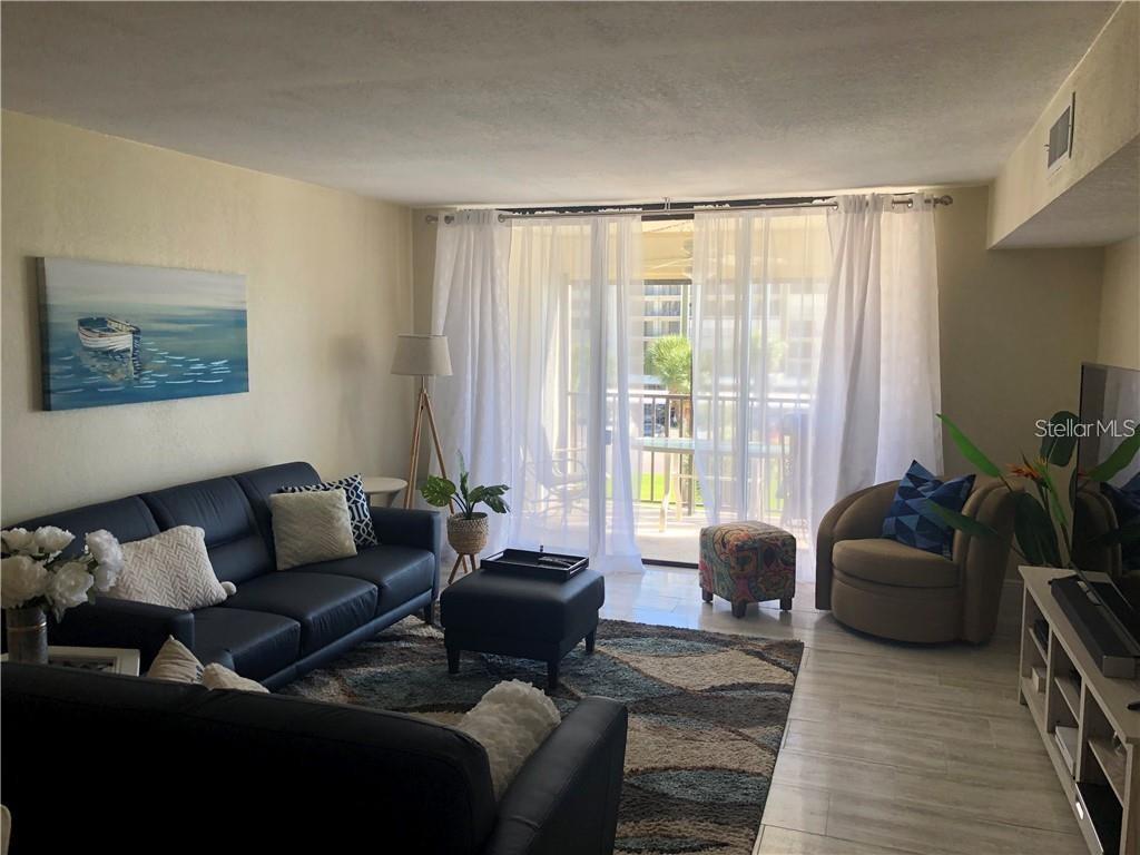 A living room features a dark leather sofa, a patterned rug, and floor-to-ceiling white curtains — 1460 GULF BOULEVARD UNIT 302, CLEARWATER, FL