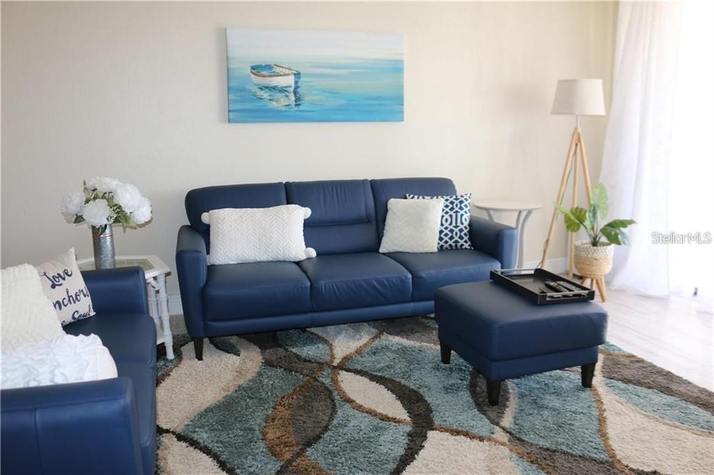 A living room features a blue leather sofa, matching ottoman, and a patterned area rug — 1460 GULF BOULEVARD UNIT 302, CLEARWATER, FL